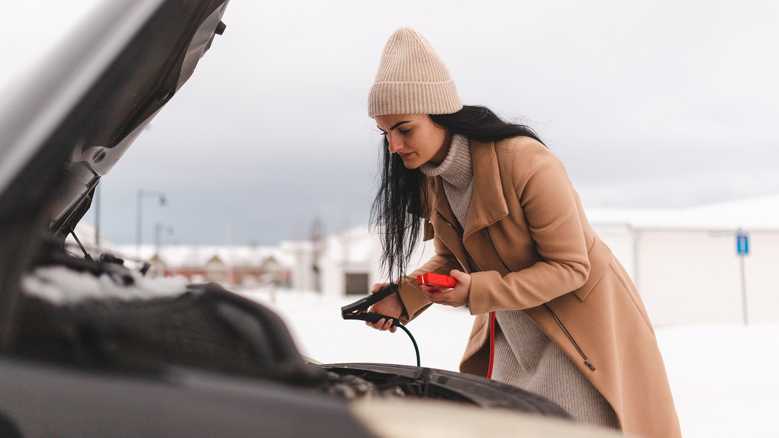 Lady stands over engine bay with jump leads